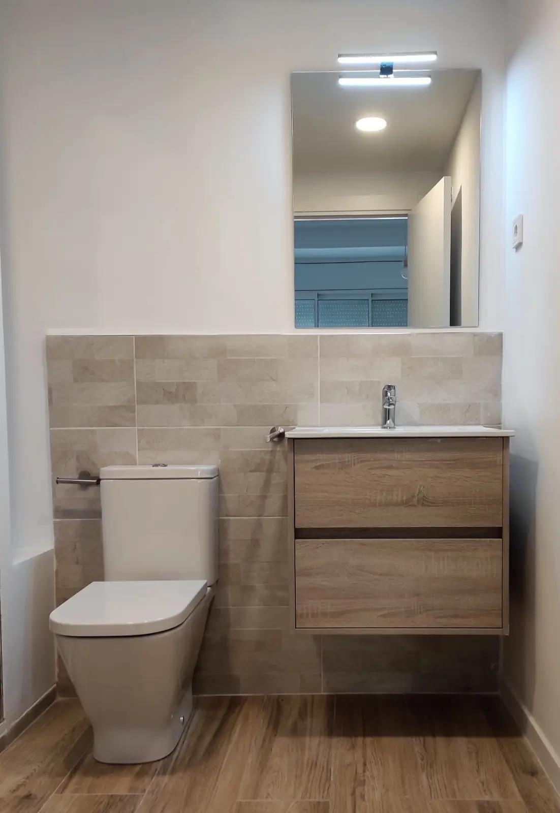 Baño con mueble de roble suspendido y revestimiento efecto piedra a media altura