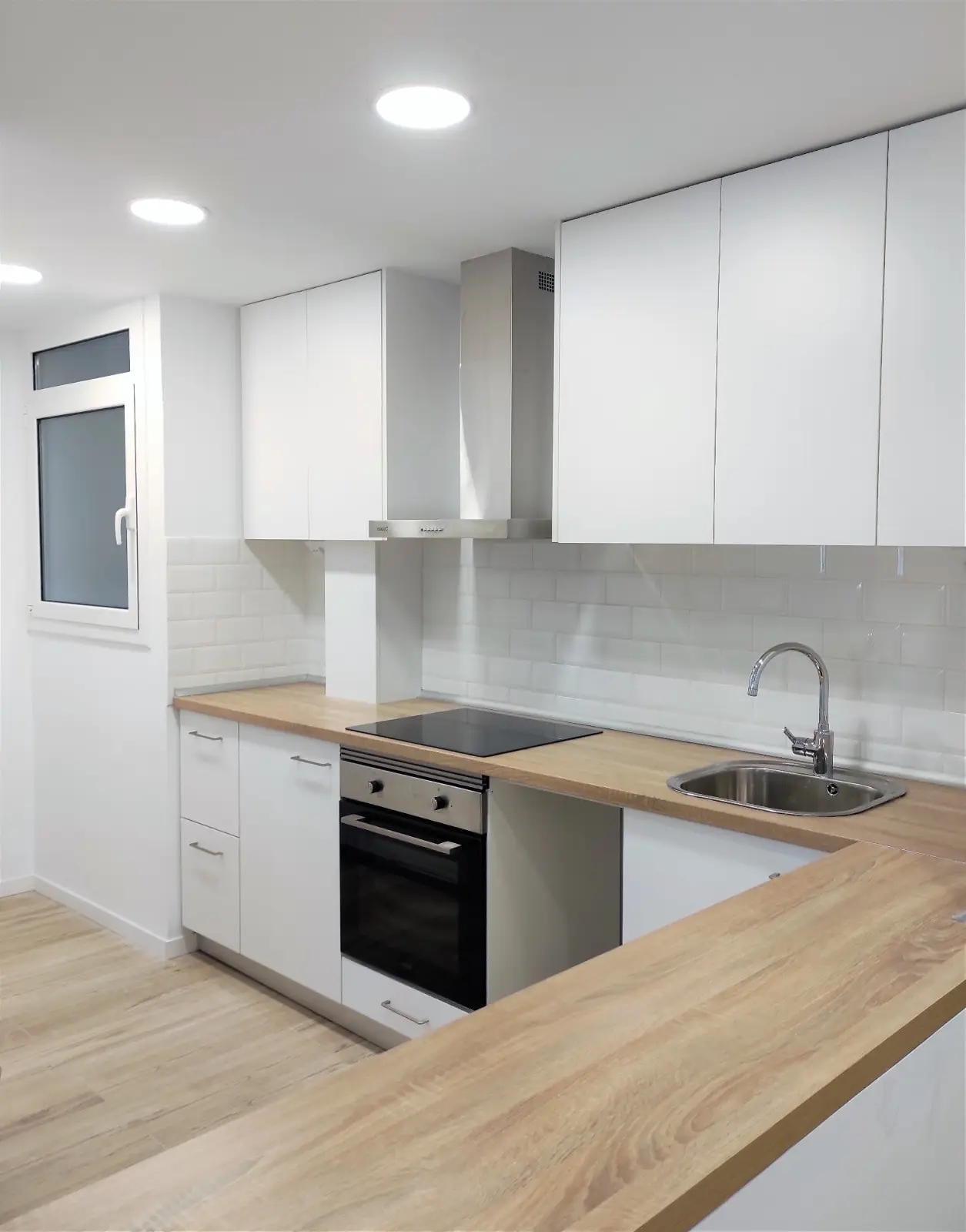 Cocina blanca en U con encimera de madera, azulejo metro y campana de acero