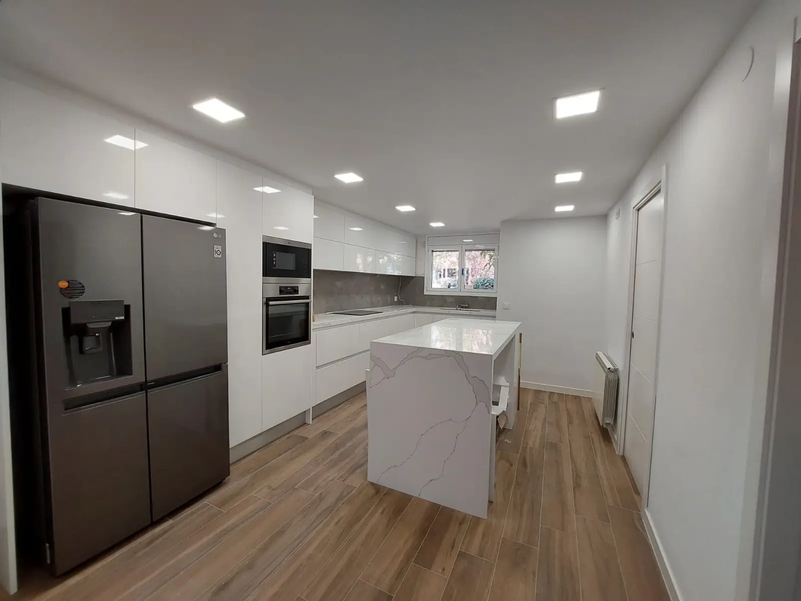 Cocina blanca brillo con isla de porcelánico efecto mármol y suelo imitación madera