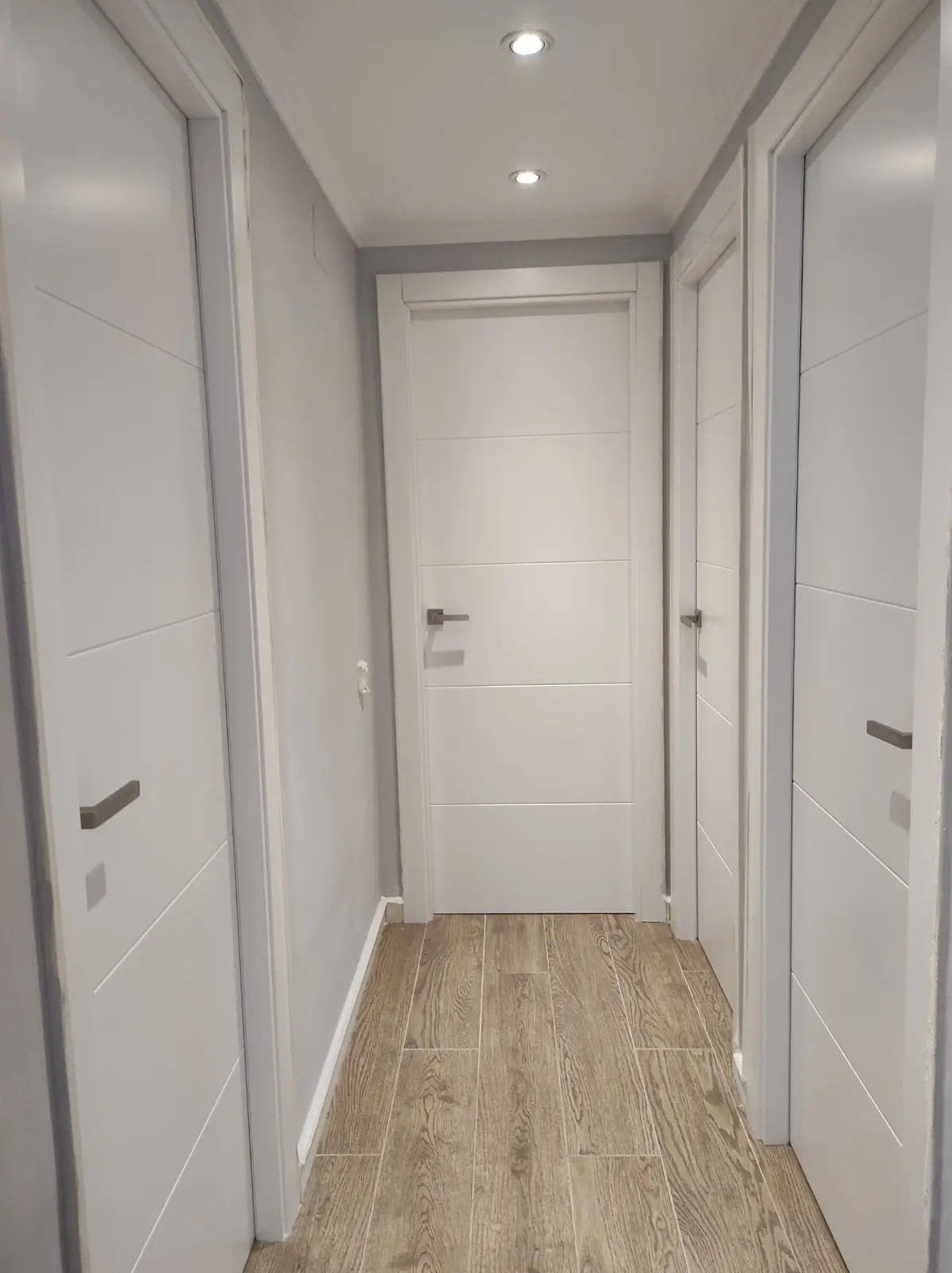 Pasillo con puertas lacadas blancas nuevas, focos empotrados y suelo porcelánico madera